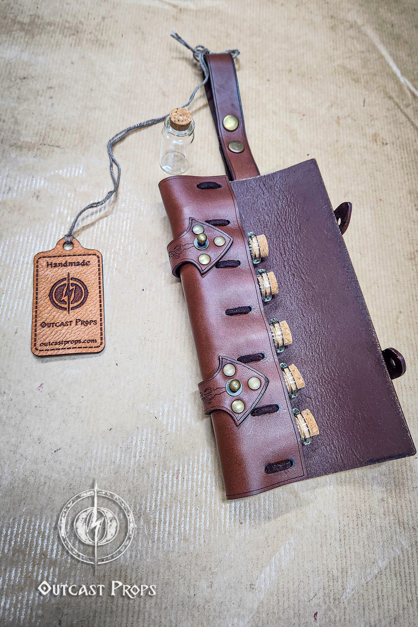 Brown leather quiver with bottle holder on a textured surface, featuring 'Outcast Props' branding. 6 Small Potion leather case, vertical belt kit for LARP, Cosplay and Costume. Easily Carry six strong cristal bottle with cork