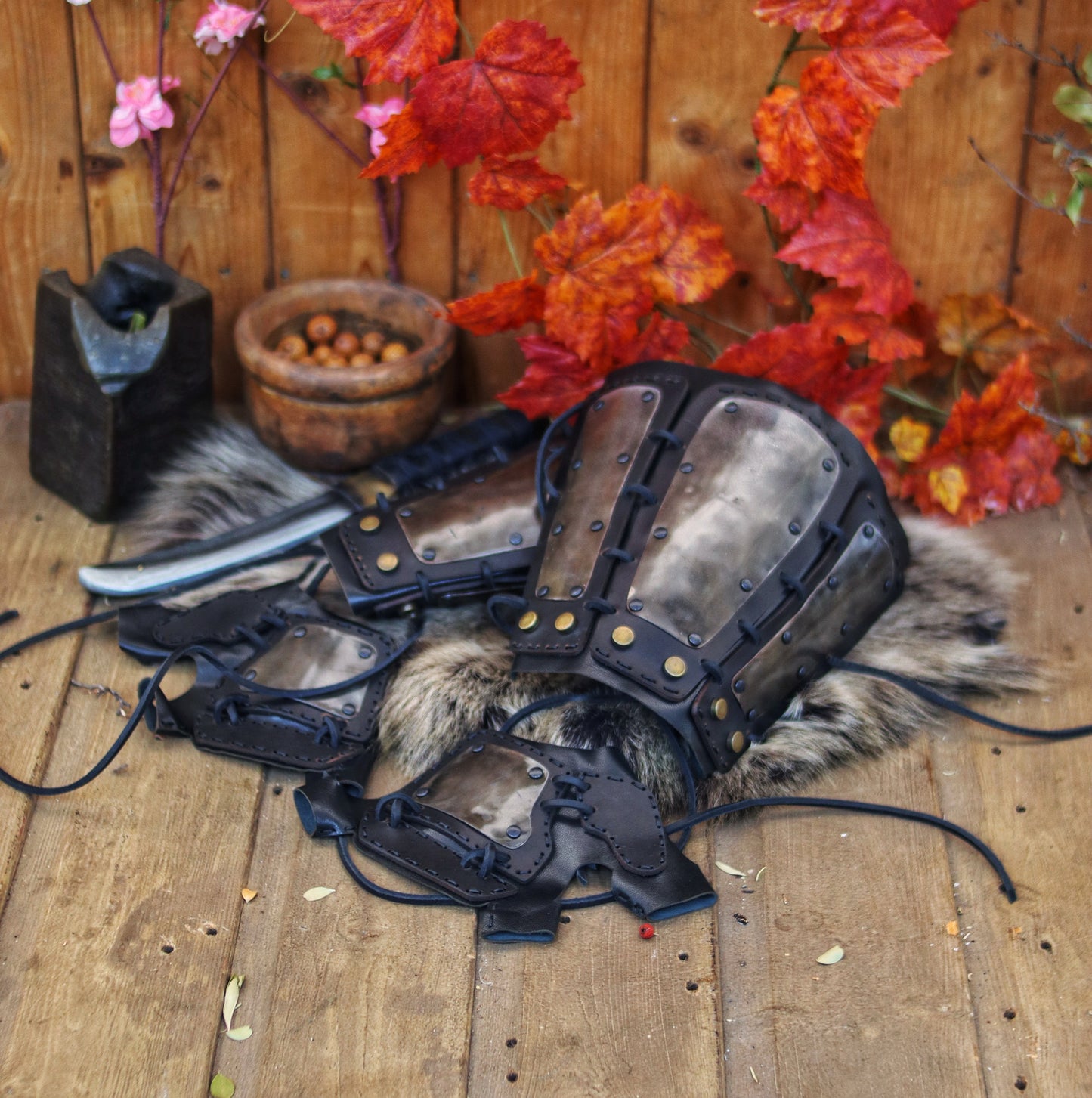 A pair of samurai armoured bracers with leather and iron components, displayed on a wooden surface with a backdrop of autumn leaves. Samurai armor iron bracers, Samurai cosplay armoured leather pair of bracers for larp, leather and Iron bracers for post apocalyptic costume