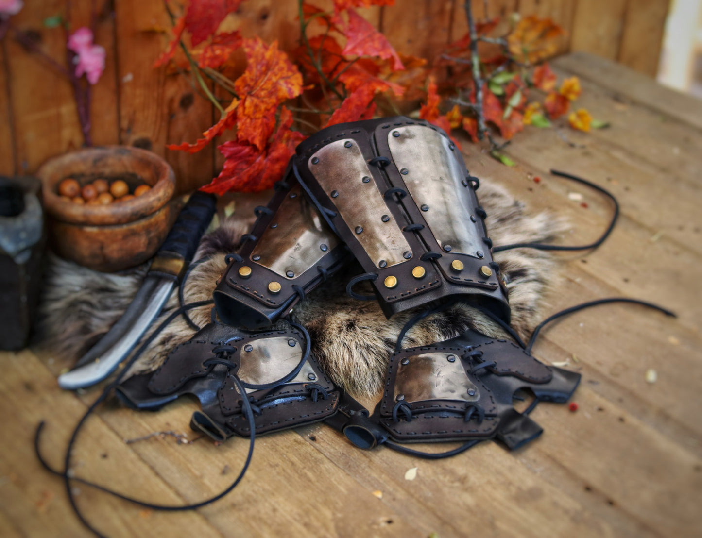 A pair of samurai armoured bracers with leather and iron components, displayed on a wooden surface with a backdrop of autumn leaves. Samurai armor iron bracers, Samurai cosplay armoured leather pair of bracers for larp, leather and Iron bracers for post apocalyptic costume