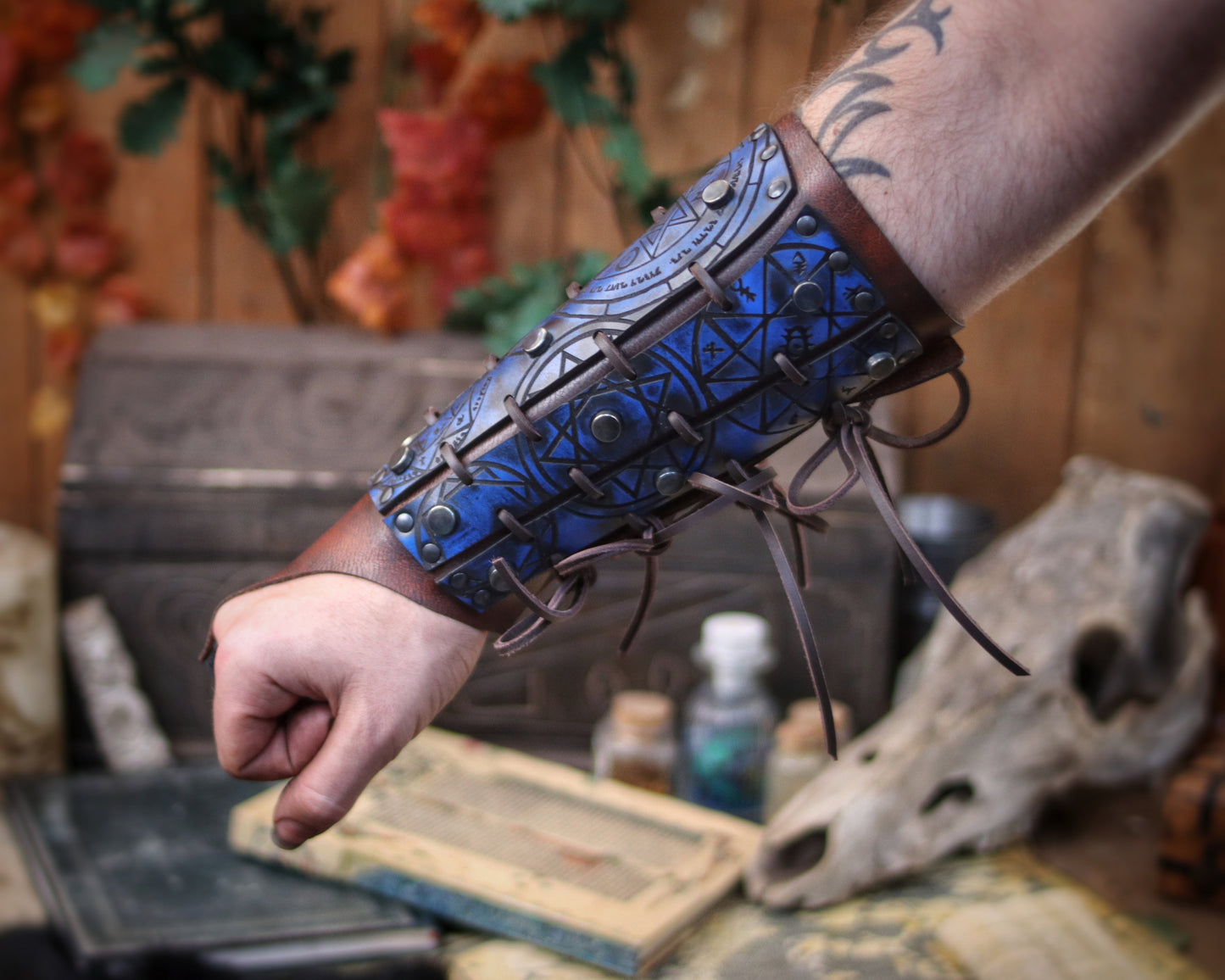 Blue leather bracer for LARP and fantasy cosplay, engraved with alchemical symbols and mystical geometry. Decorated with metal studs and polished beads for a gothic warlock or dark wizard look. Handmade from vegetable-tanned Spanish leather, adjustable and resistant. Perfect for witches, ritualists, or demon hunters in immersive fantasy roleplay.