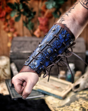 Blue leather bracer for LARP and fantasy cosplay, engraved with alchemical symbols and mystical geometry. Decorated with metal studs and polished beads for a gothic warlock or dark wizard look. Handmade from vegetable-tanned Spanish leather, adjustable and resistant. Perfect for witches, ritualists, or demon hunters in immersive fantasy roleplay.