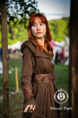 Person in a brown costume holding a bow and arrow, with a blurred outdoor background. Viking Leather Bracers with Norse Knot Engraving for LARP Cosplay Medieval Fantasy Roleplay Handmade Armor Custom Gear for Men or Women