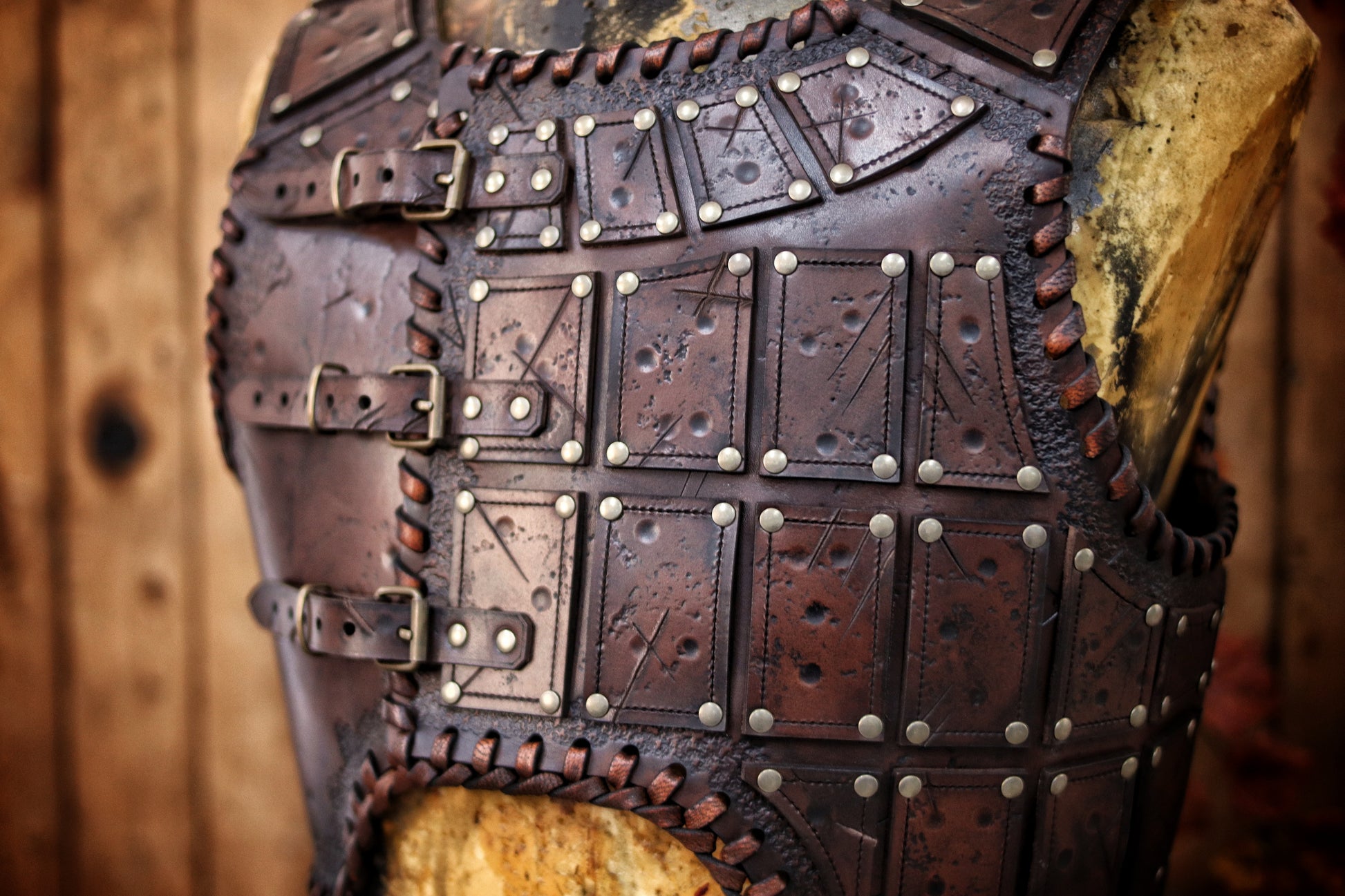 A handmade leather studded armor displayed on a wooden stand with a fur cape, featuring brown leather plates with studs, and a corded edge finish. Barbarian studded leather chest armor with rabbit fur cape attachment shown on mannequin. Perfect for fantasy LARP, Viking reenactment or cosplay, this full-grain leather armor is aged by hand and paired here with fur for an epic look. Adjustable buckle straps and visible stitching add to the rugged charm of this high-impact warrior costume piece.