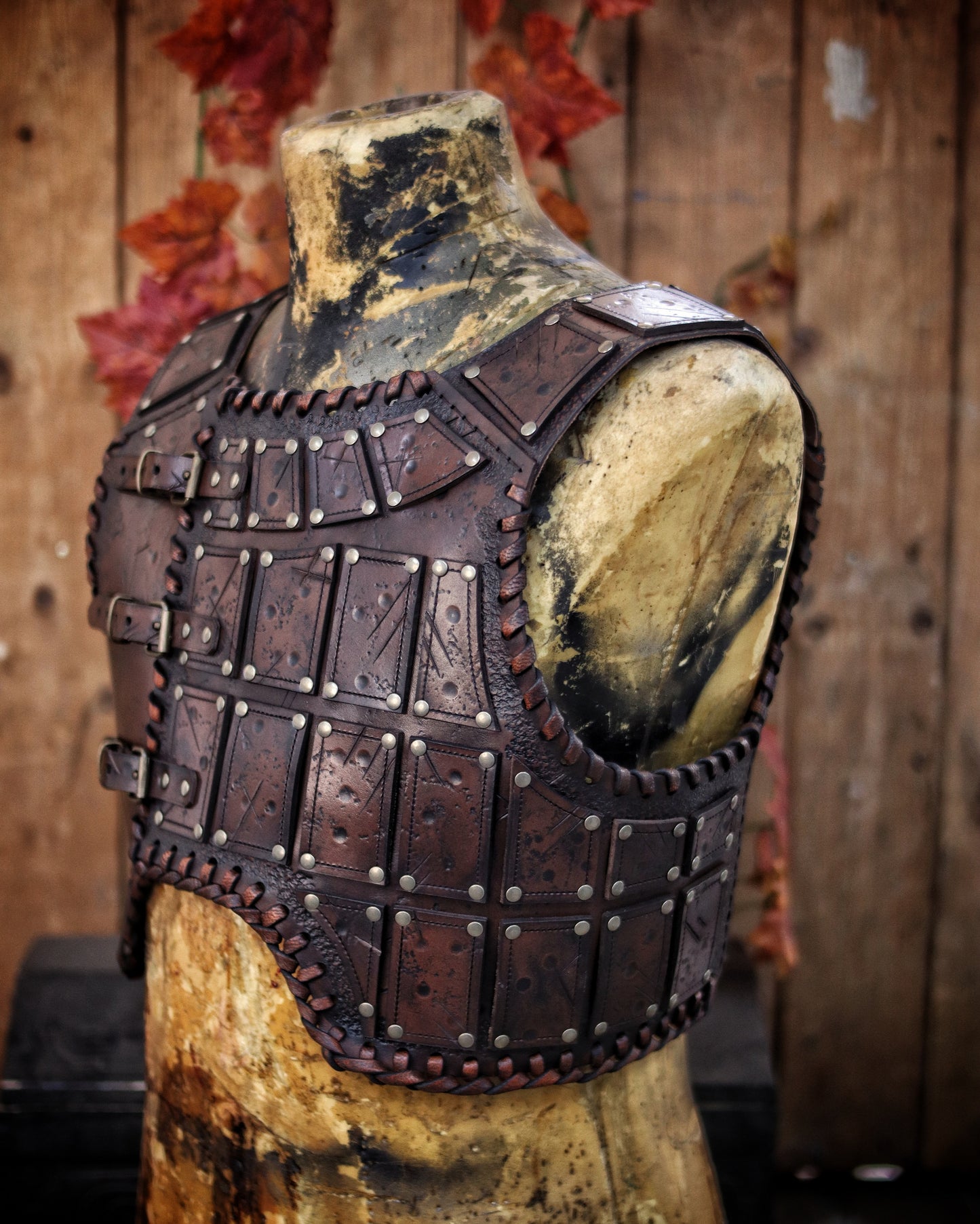 A handmade leather studded armor displayed on a wooden stand with a fur cape, featuring brown leather plates with studs, and a corded edge finish. Barbarian studded leather chest armor with rabbit fur cape attachment shown on mannequin. Perfect for fantasy LARP, Viking reenactment or cosplay, this full-grain leather armor is aged by hand and paired here with fur for an epic look. Adjustable buckle straps and visible stitching add to the rugged charm of this high-impact warrior costume piece.
