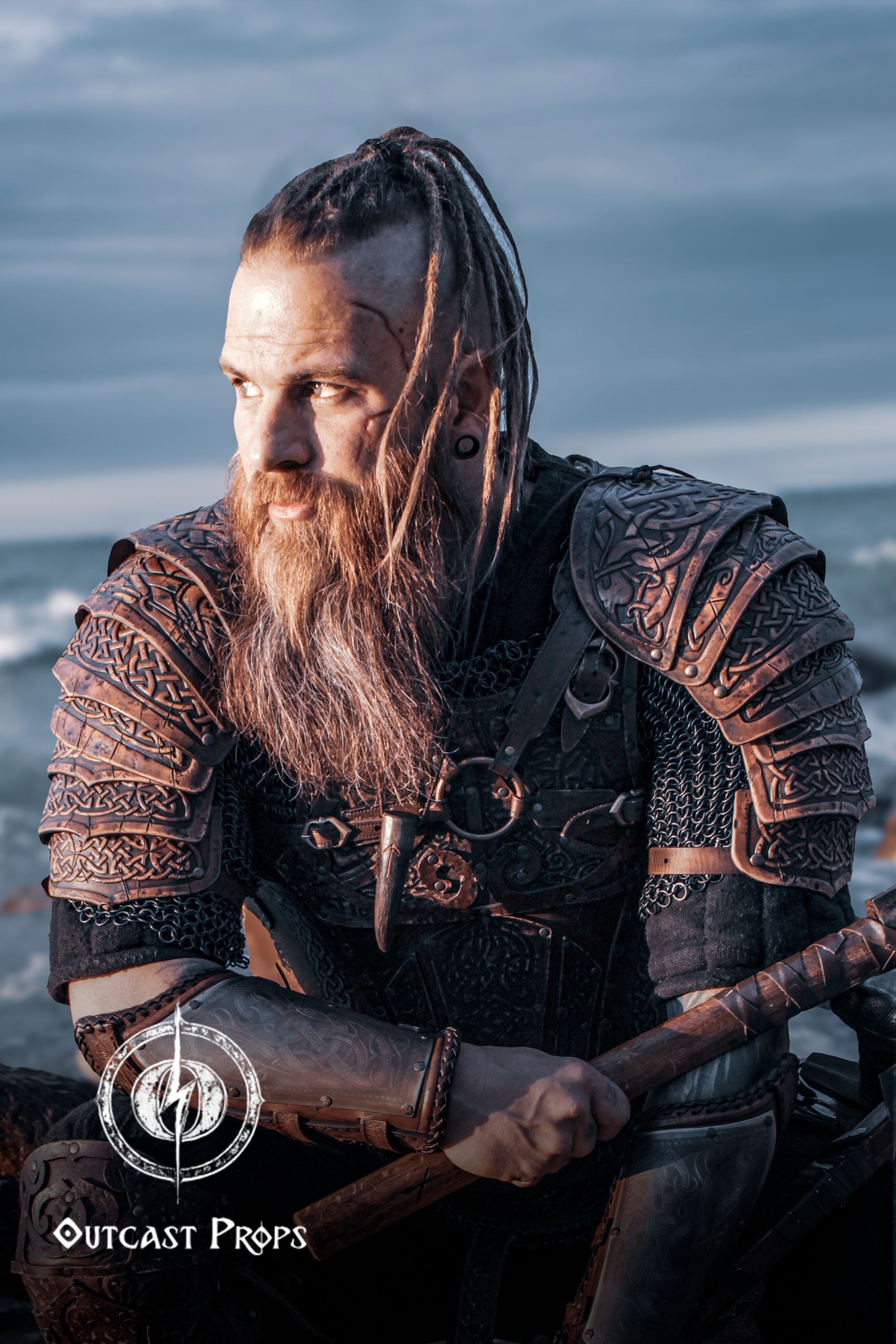 Bearded LARP warrior in full viking leather shoulder armor Sedrik, seated by the sea at sunset. The engraved Nordic pauldrons with layered leather plates feature detailed Celtic knots and fold for full mobility. Ideal for viking cosplay shoulder armor, Nordic warrior LARP gear, celtic leather pauldrons for fantasy costumes or medieval shoulder armor for immersive roleplay and conventions