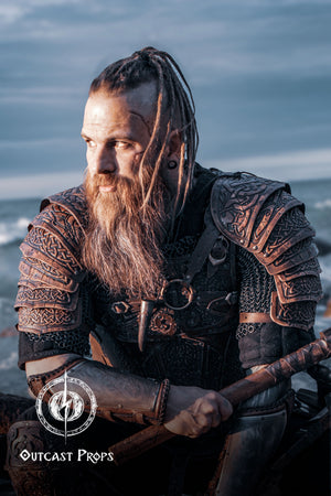 Bearded LARP warrior in full viking leather shoulder armor Sedrik, seated by the sea at sunset. The engraved Nordic pauldrons with layered leather plates feature detailed Celtic knots and fold for full mobility. Ideal for viking cosplay shoulder armor, Nordic warrior LARP gear, celtic leather pauldrons for fantasy costumes or medieval shoulder armor for immersive roleplay and conventions