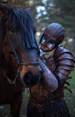 Viking warrior in full handcrafted Celtic leather armor Sedrik, detailed with Nordic knot engravings and fantasy Viking leather shoulder pauldrons, photographed outdoors petting a brown horse. Helmet with engraved leather and face paint complete the Nordic LARP armor look. Ideal for Viking cosplay, fantasy LARP armor, Norse warrior costume, Viking leather armor set, horse-mounted warrior outfit, Nordic reenactment, and Celtic fantasy costume. Premium leather craftsmanship and textures.