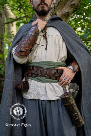 Person in medieval attire holding leather quivers with 'Outcast Props' logo.