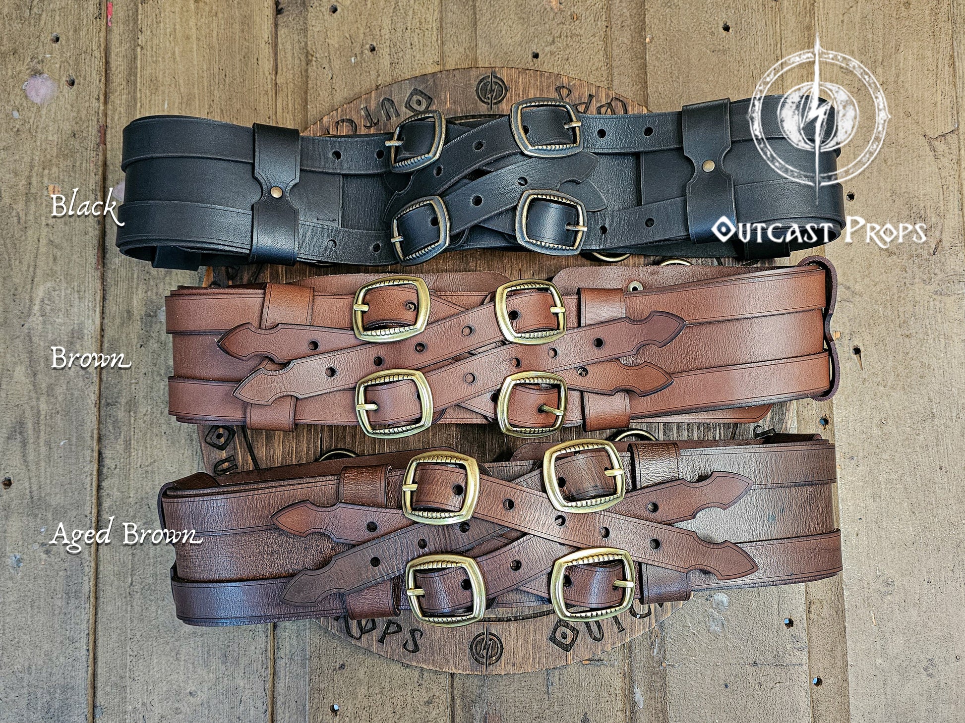 Adventurer Leather Belt for LARP, Pirate Belt, Alchemist Belt, Medieval Belt, Fantasy, Steampunk, Wide Leather Belt, Adjustable Belt. Three leather belts in black, brown, and aged brown on a wooden background with 'Outcast Props' branding.