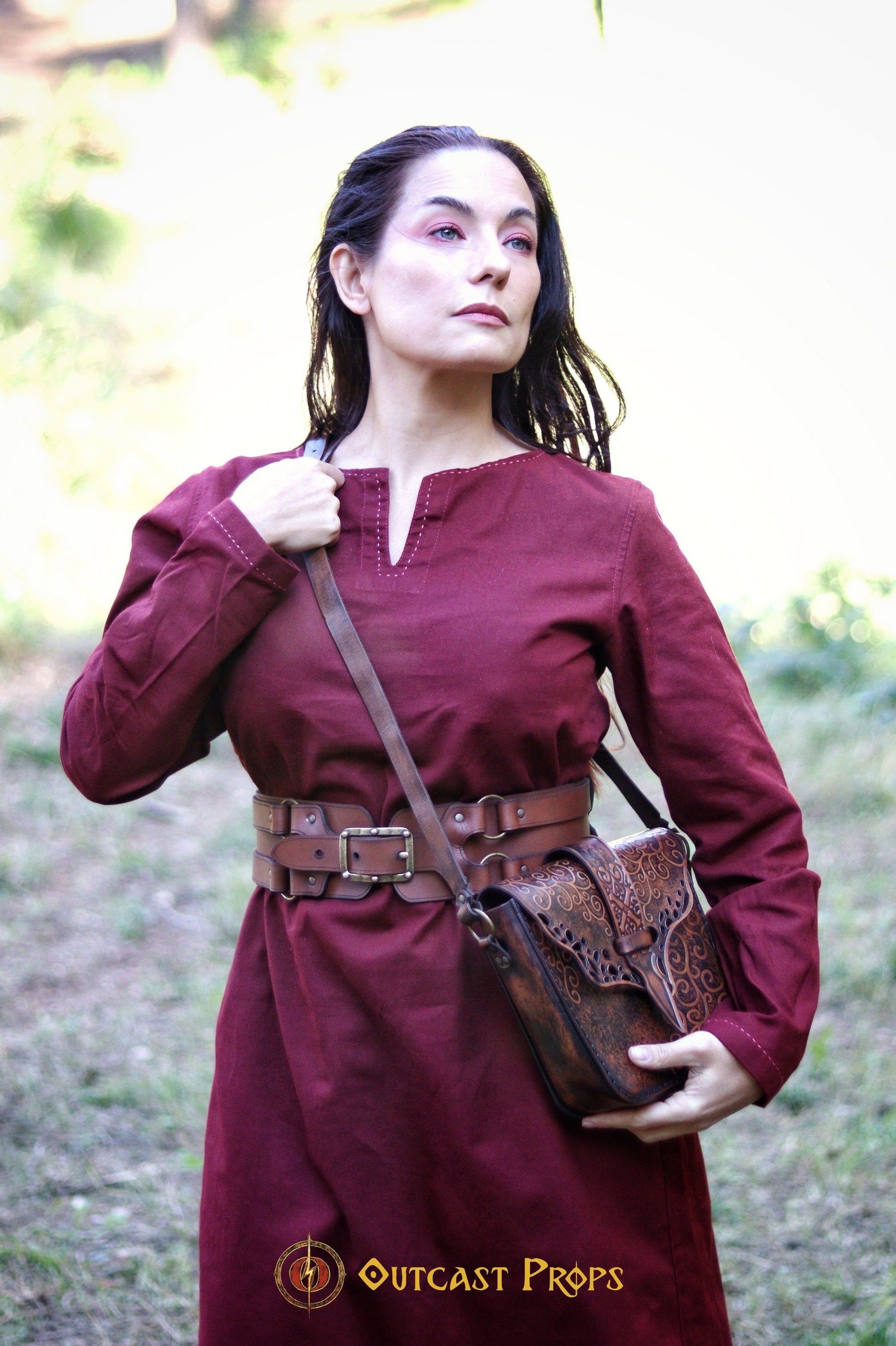 Close-up of a woman in a burgundy medieval tunic wearing the Adventurer Leather Belt for LARP, with an embossed leather alchemist pouch over her shoulder. This wide leather belt for cosplay fits snugly around her waist, showing the high-quality handcrafted detailing. A perfect steampunk and fantasy belt for LARP characters, ideal for organizing gear like potion vials, scrolls, and tools while staying stylish.