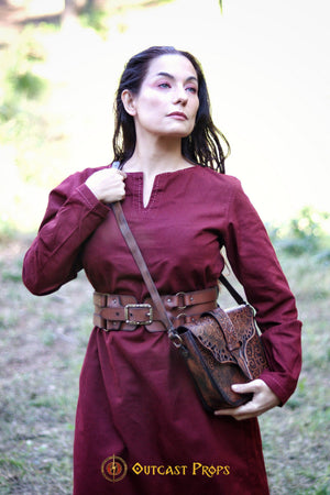 Close-up of a woman in a burgundy medieval tunic wearing the Adventurer Leather Belt for LARP, with an embossed leather alchemist pouch over her shoulder. This wide leather belt for cosplay fits snugly around her waist, showing the high-quality handcrafted detailing. A perfect steampunk and fantasy belt for LARP characters, ideal for organizing gear like potion vials, scrolls, and tools while staying stylish.
