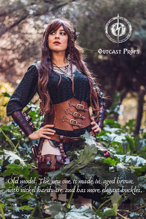Female LARP witch wearing the old version of the leather underbust corset by Outcast Props. The updated design is made in aged brown leather with nickel hardware and more elegant buckles. Perfect for ren faire outfits, fantasy costumes, and steampunk waist cincher looks. Handcrafted from vegetable-tanned leather, this corset embodies artisanal craftsmanship for witches and alchemists.