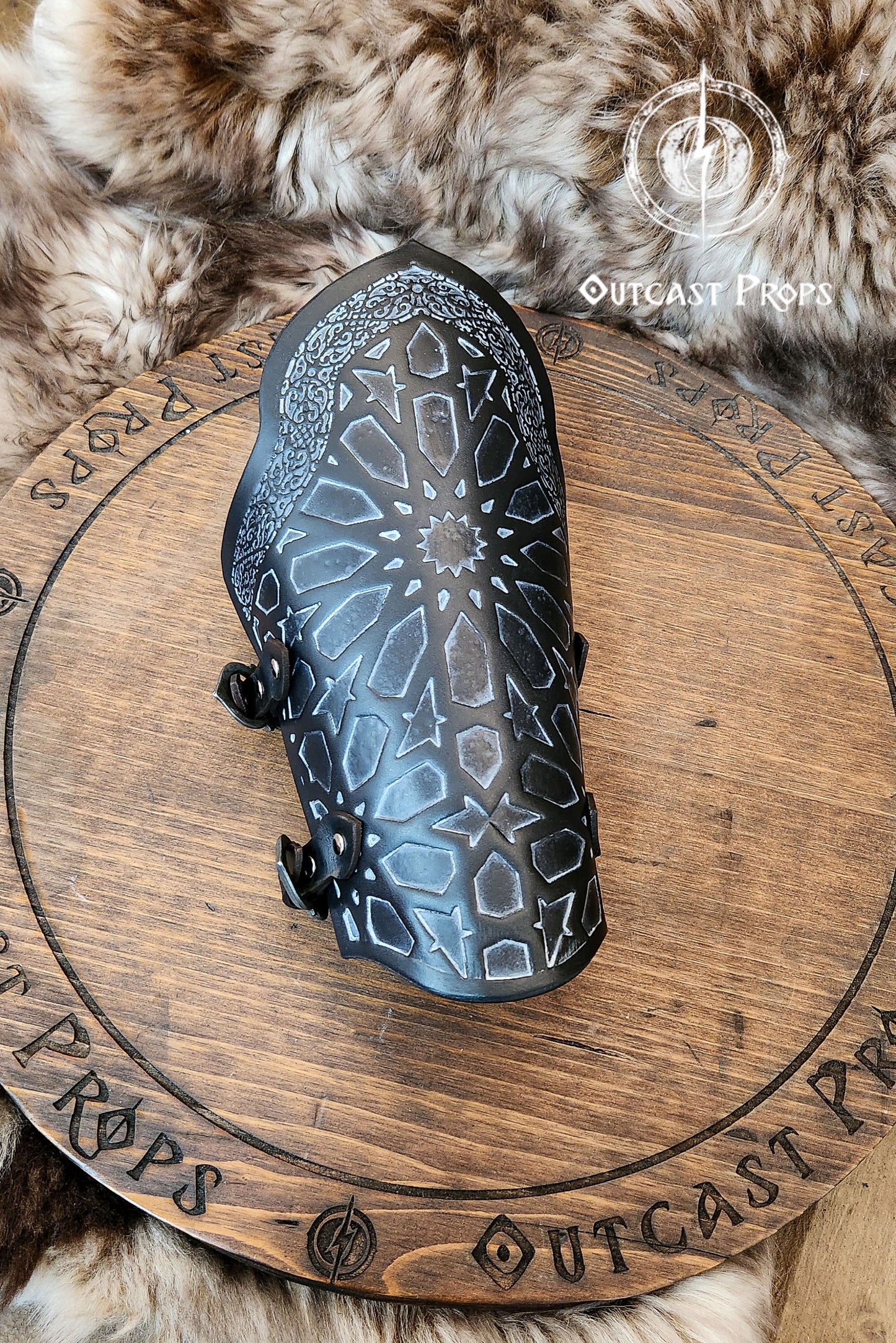 Artistic still life of a pair of black leather bracers with Arabic geometric design, resting on a wooden ritual board surrounded by oriental props like a lantern, tea set, and potion bottles. These assassin leather bracers are ideal for LARP costumes, fantasy rogue armor, and cosplay gear with oriental inspiration. The engraved surface highlights Islamic motifs, while the scene evokes a magical assassin’s den, making the bracers both decorative and practical in use.