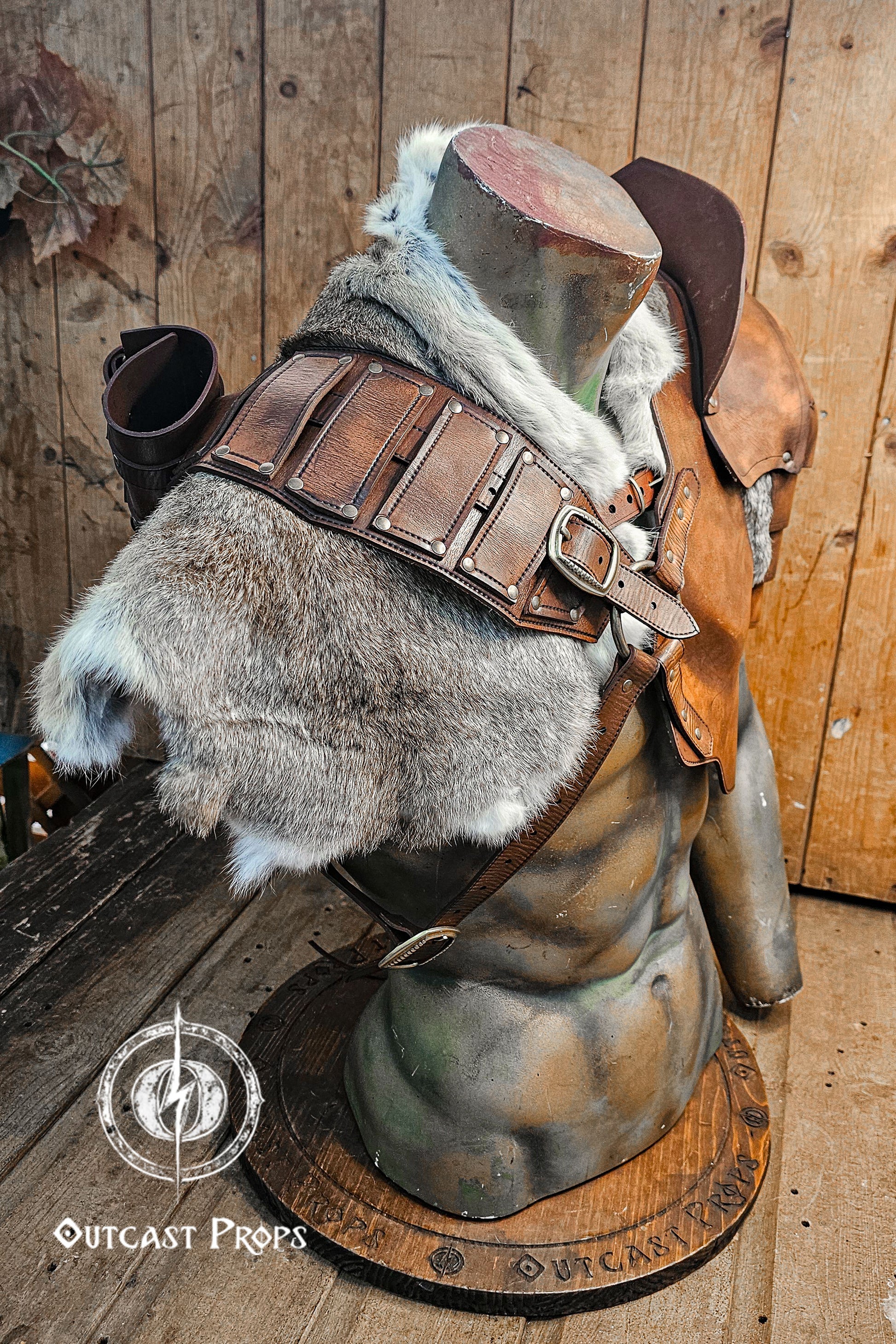 Angle view from behind highlighting the fur mantle secured with reinforced leather straps over a harness system. Visible potion or scroll holder attached at the back. Ideal for LARP or fantasy warriors in need of versatile costume pieces. The aged brown vegetable-tanned leather is distressed with Outcast Props’ signature finish, giving it an authentic cinematic battle-worn effect.