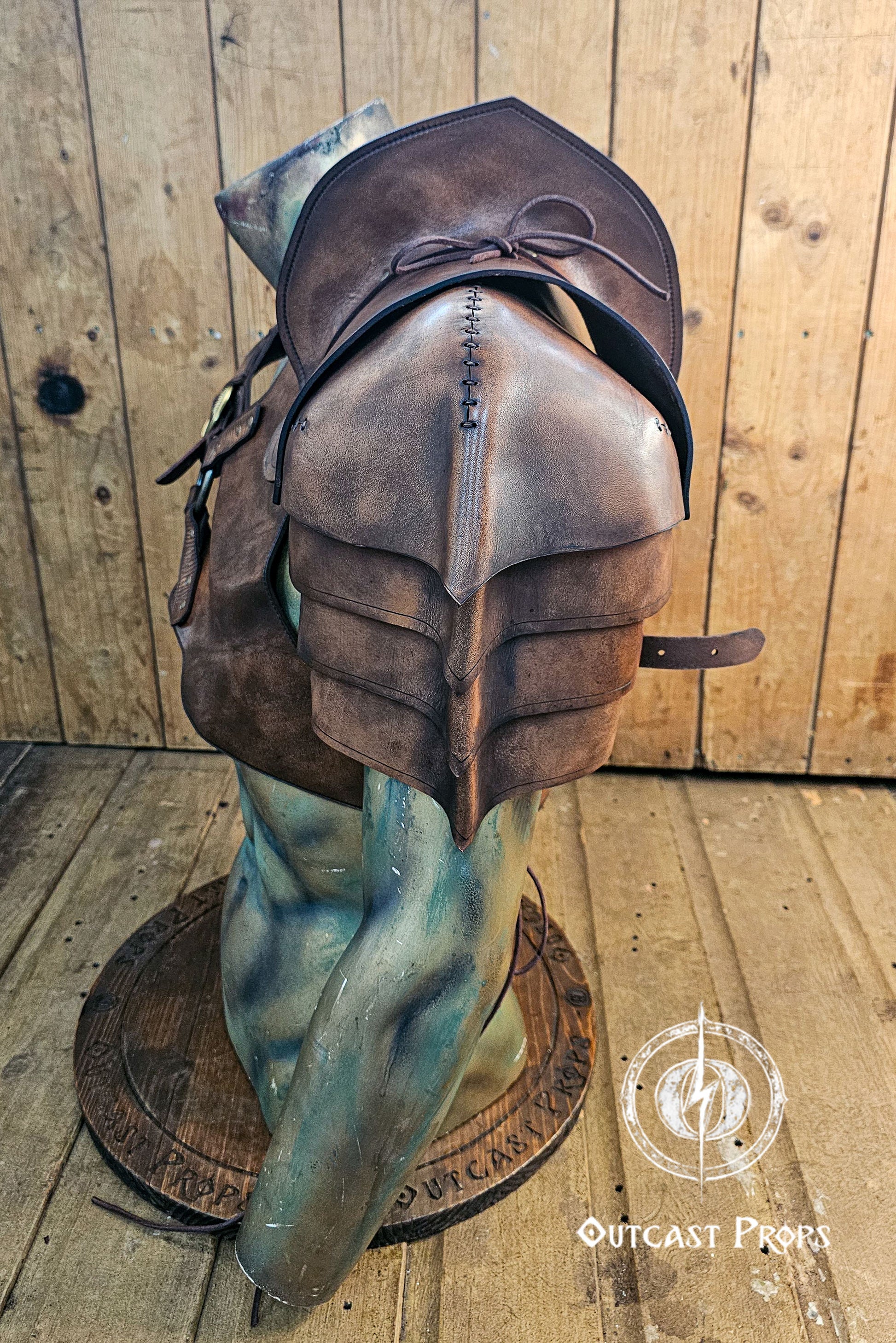 Close-up of the brown barbarian leather shoulder armor showing the riveted construction and embossed weathered surface. The layered shoulder pieces are attached to a central harness with metal buckles and straps. Visible aged patina highlights the artisan leatherwork. Ideal for viking warrior costume, larp armor for men, or fantasy cosplay. Sword sheath partially visible on the back.