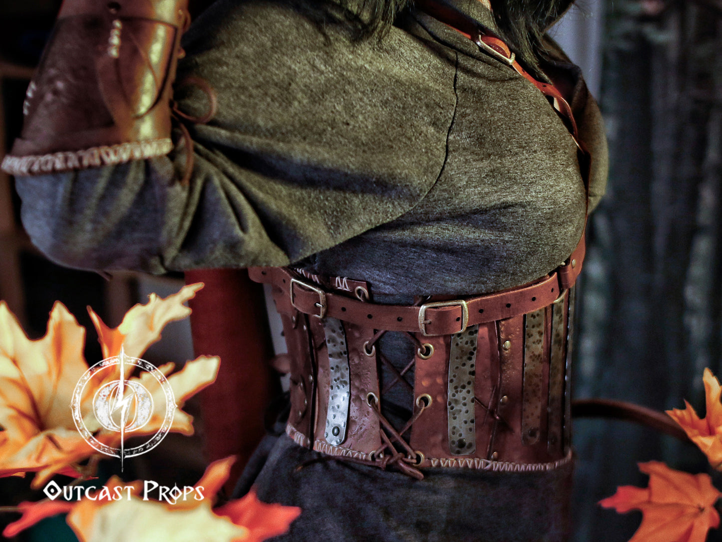 Person wearing a detailed leather belt with metal accents, standing against a dark background with autumn leaves. Barbarian Leather armor woman, larp armor woman viking piece woman post apocalyptic cosplay