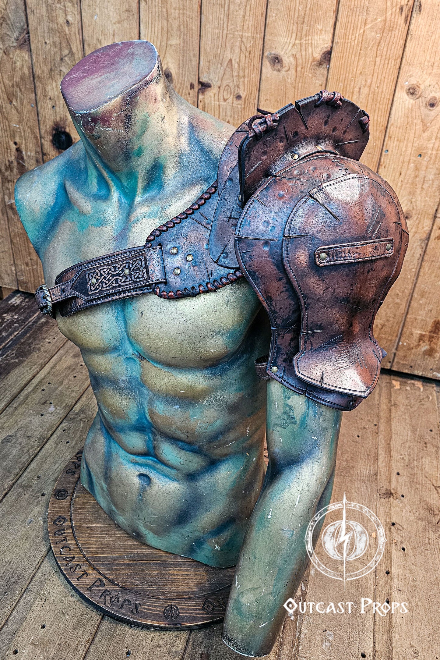 Barbarian Viking Leather Shoulder armor set. Mannequin torso with armor and helmet on a wooden floor, Outcast Props brand visible