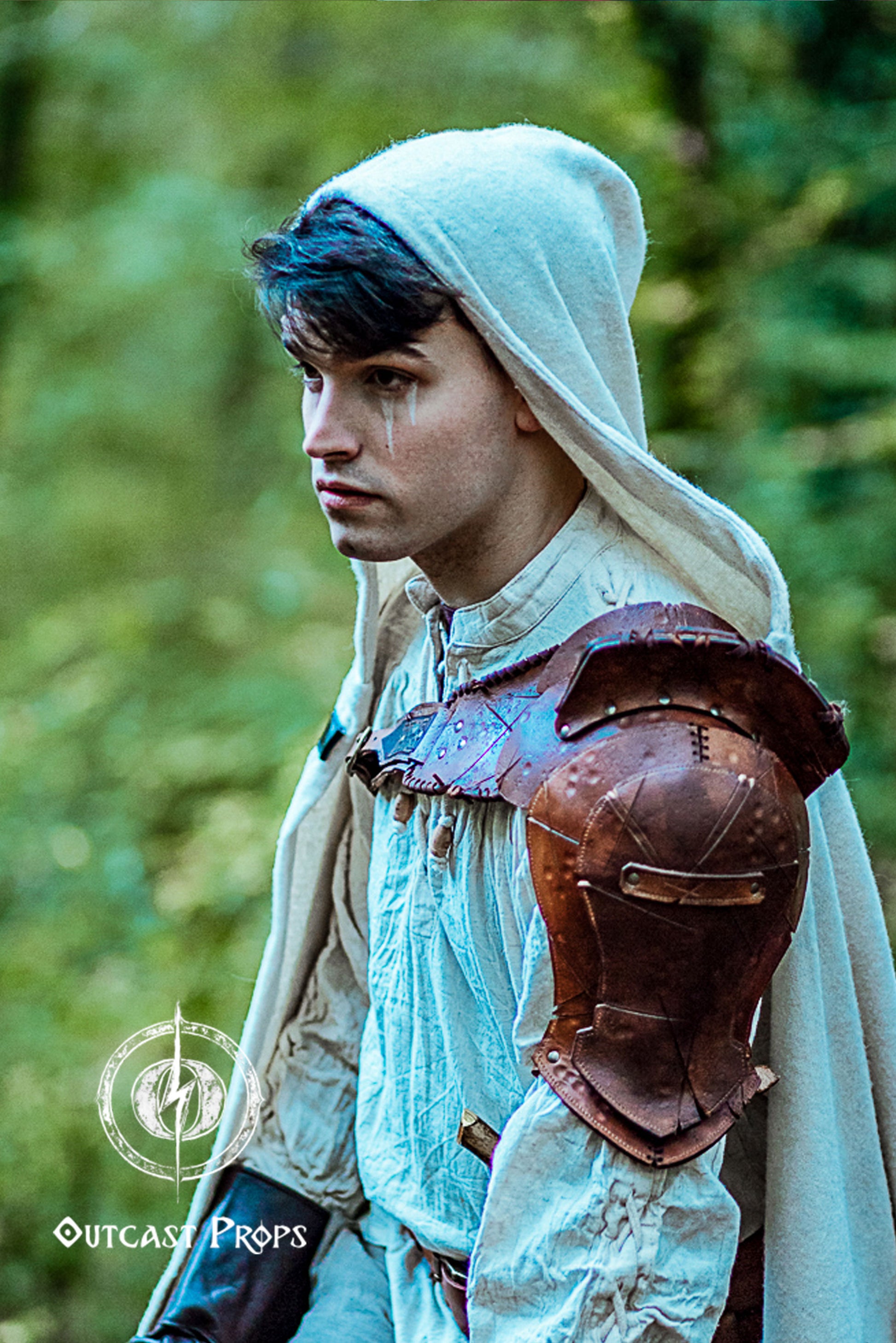 Barbarian Viking Leather Shoulder armor set. Person in medieval or fantasy attire with a hooded cloak and leather shoulder guard, standing outdoors.