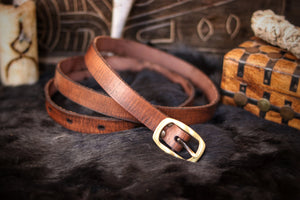 A brown leather belt with a buckle, placed on a furry surface, with props and a storage box in the background. 20 Plain leather belt