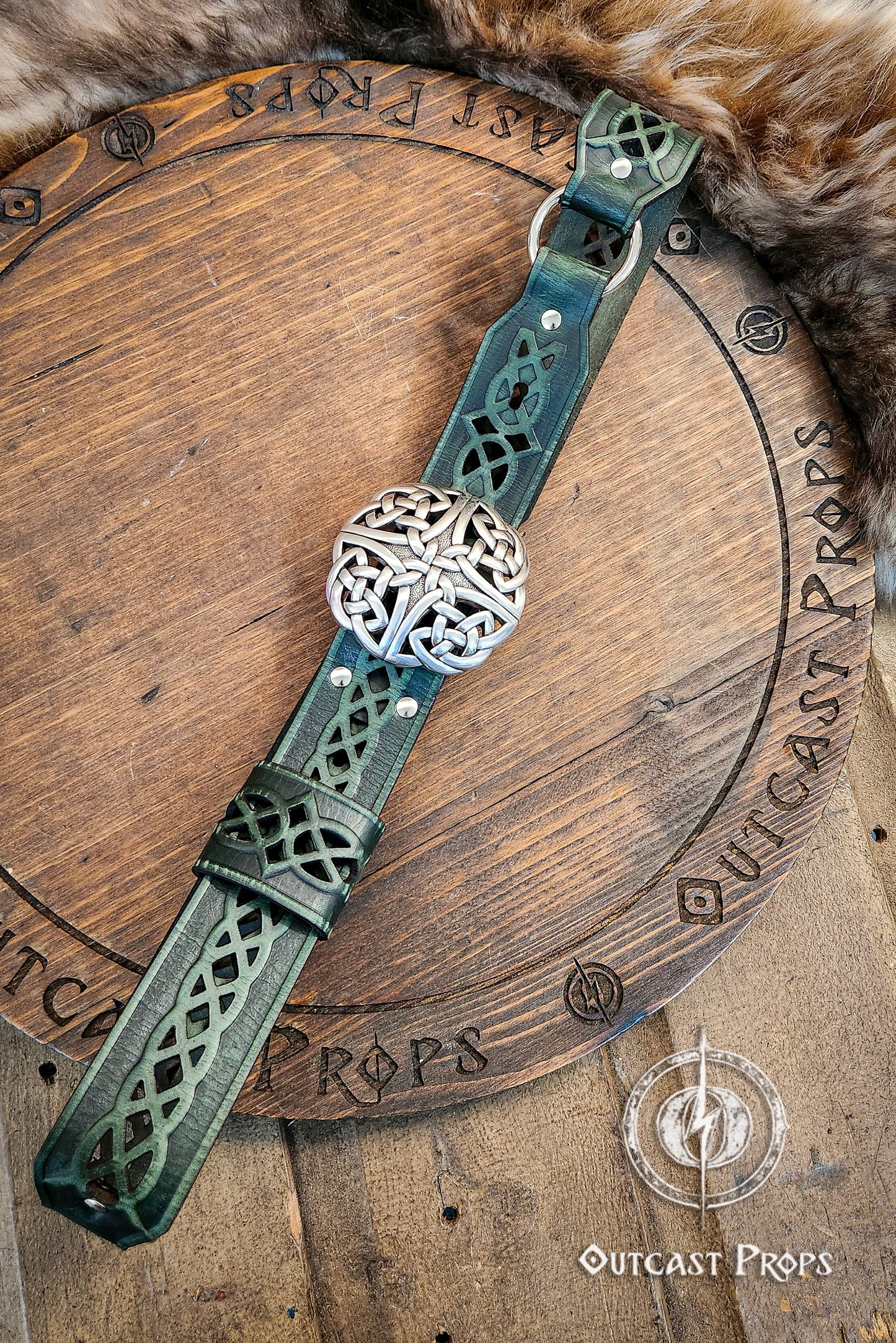 Decorative leather strap with metal ball on a wooden surface, branded 'Outcast Props'.