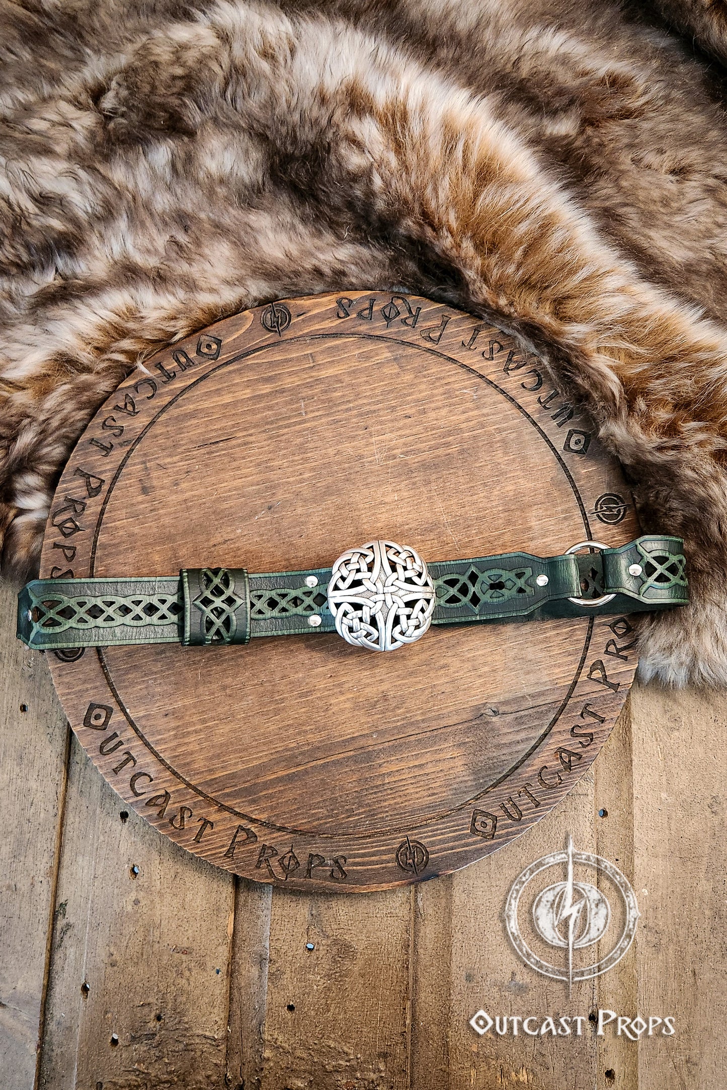 Wooden shield with a decorative belt on a fur and wooden background, branded 'Outcast Props'.