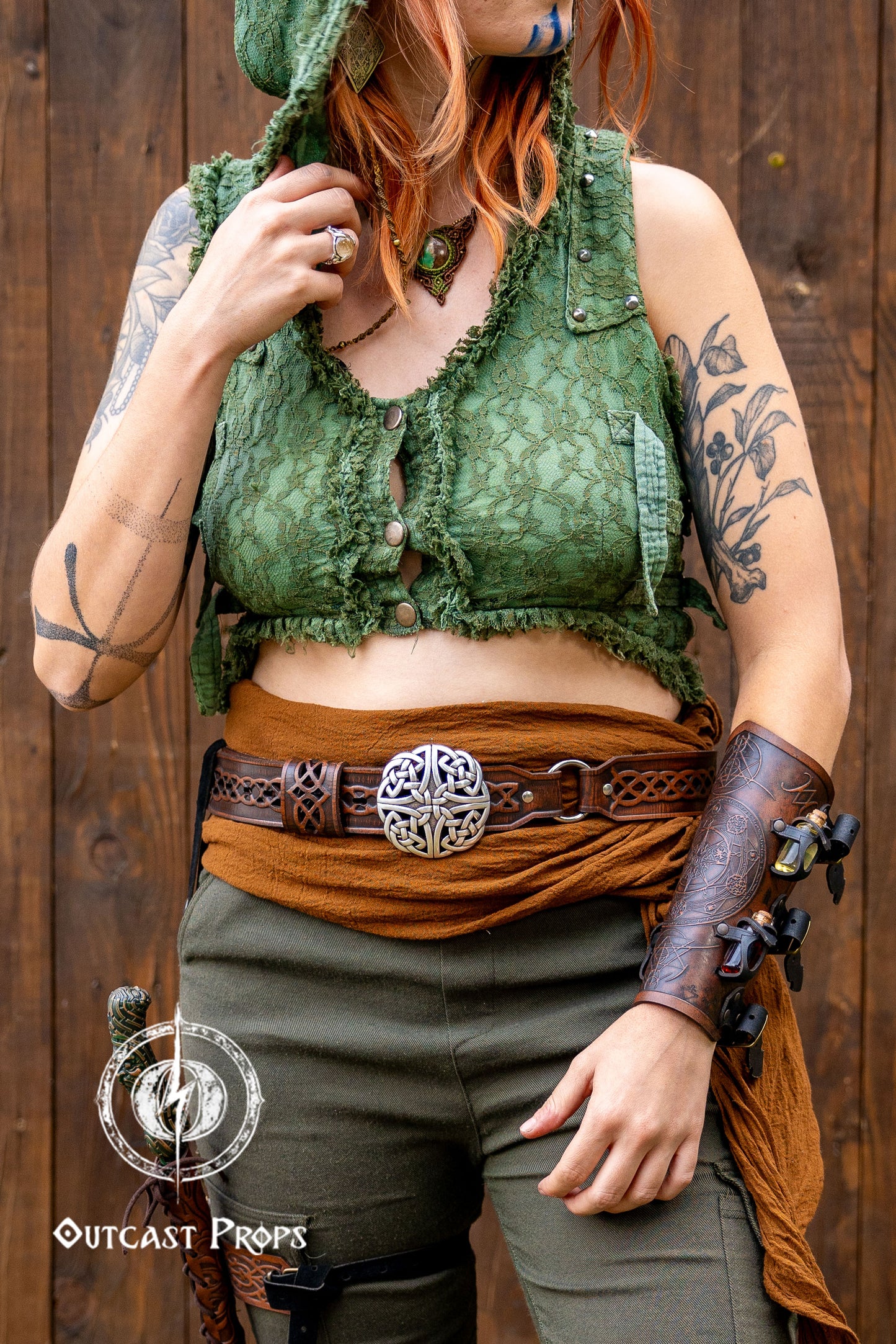 Person wearing a green top and brown skirt with tattoos and accessories against a wooden background. Celtic knot leather belt silver buckle larp belt for ren fair fantasy costume celtic belt unisex leather belt for renaissance outfit
