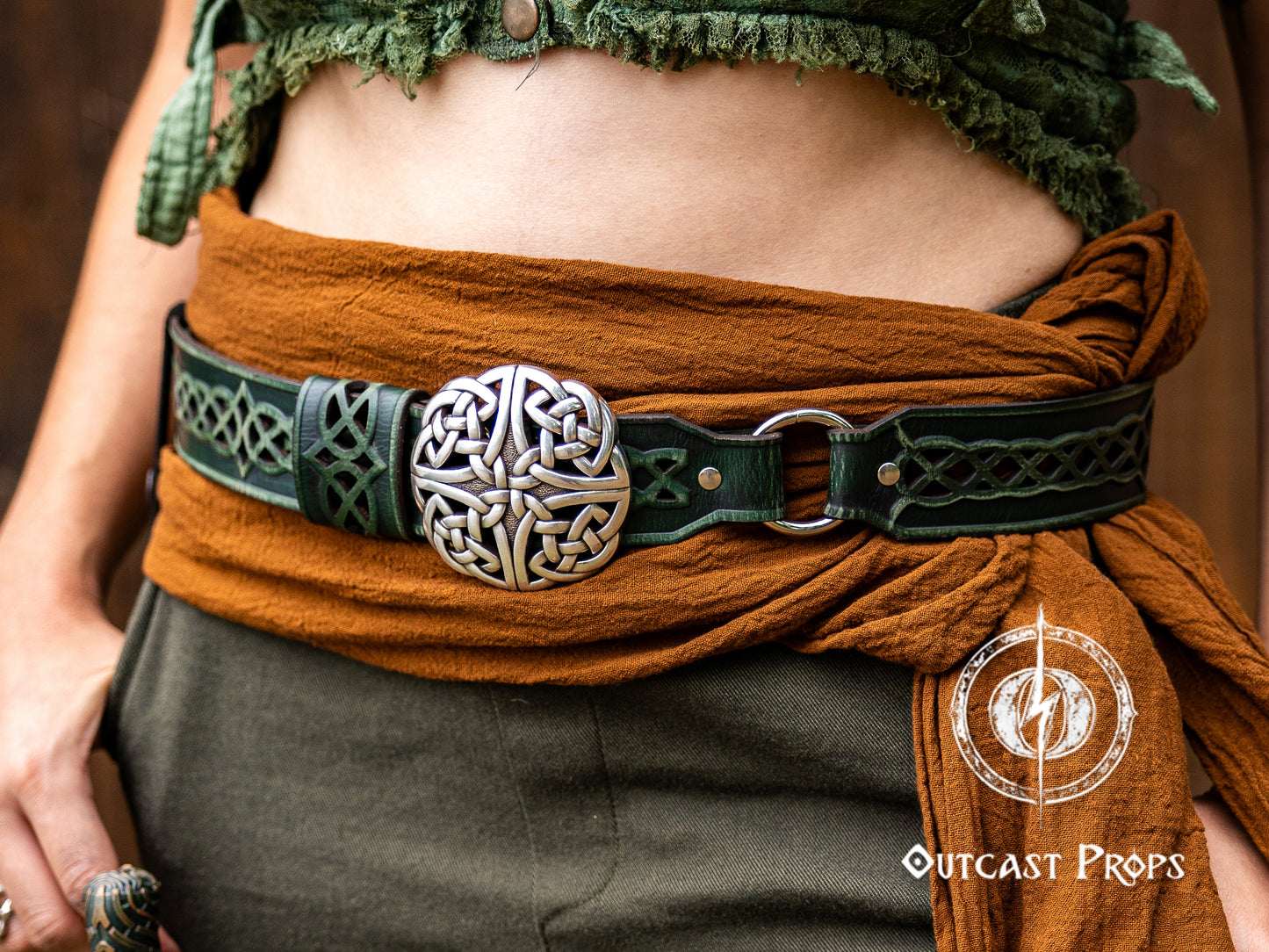Person wearing a brown belt with a decorative buckle, featuring Outcast Props branding. Celtic knot leather belt silver buckle larp belt for ren fair fantasy costume celtic belt unisex leather belt for renaissance outfit