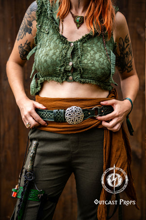 Person wearing a green top and brown pants with a belt, holding a weapon, against a brown background. Celtic knot leather belt silver buckle larp belt for ren fair fantasy costume celtic belt unisex leather belt for renaissance outfit