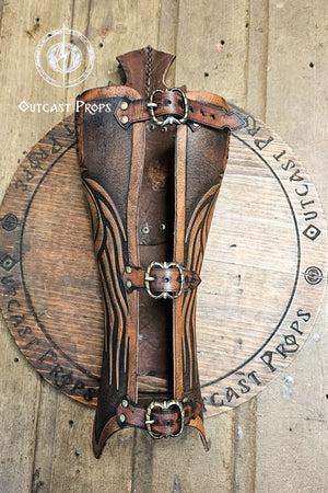 Aged brown Celtic leather greave handcrafted from full-grain vegetable-tanned leather with embossed flowing Nordic lines and three brass buckles. This medieval leg armor evokes Rohirrim horsemen and Viking warriors, combining authentic craftsmanship and durability for LARP and fantasy cosplay. The battle-worn finish and epic painting give each greave a heroic, cinematic look ideal for riders and explorers.