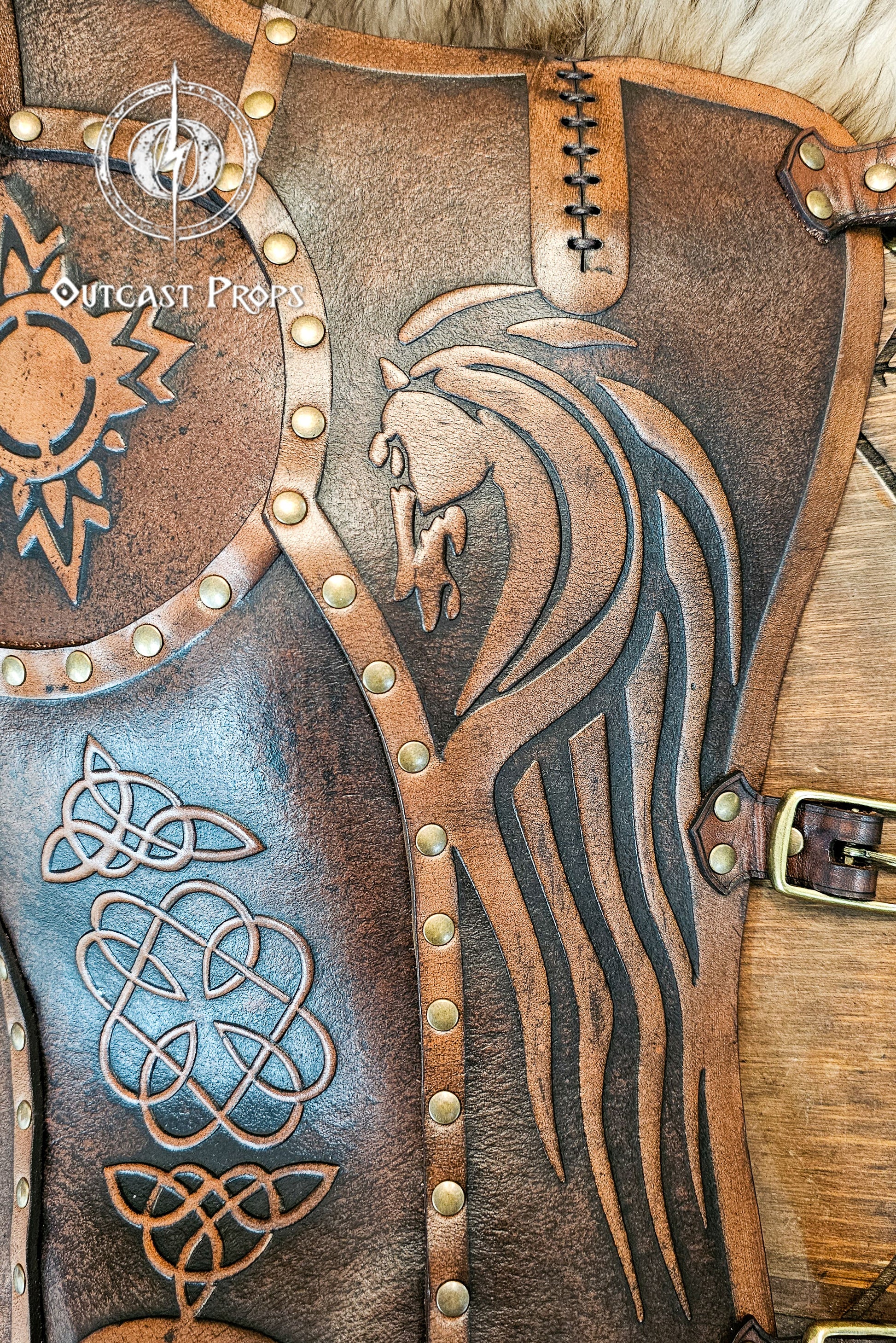 Close-up of aged brown Celtic leather greave handcrafted from full-grain vegetable-tanned leather, showing a detailed embossed horse motif inspired by the Rohirrim riders of Middle-earth. Surrounded by Celtic knotwork and brass rivets, it captures the essence of Viking and medieval craftsmanship. Ideal for LARP armor, fantasy horsemen, or reenactment costumes that demand authentic handmade detailing.