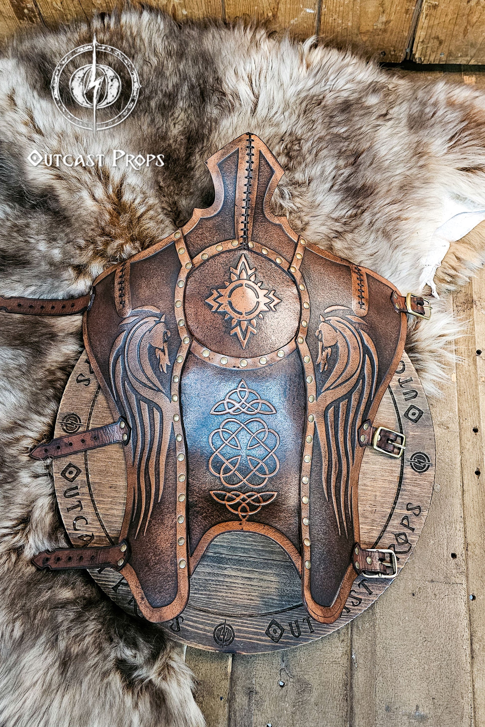 Full view of Celtic leather greaves with twin embossed horses and Celtic knotwork, crafted from aged brown vegetable-tanned leather with brass hardware. The design evokes the proud armor of Rohirrim riders and Viking warriors, resting on fur for a rustic medieval look. Perfect for LARP, cosplay, or fantasy horsemen seeking durable handmade leg armor with cinematic aged patina and artisan craftsmanship.