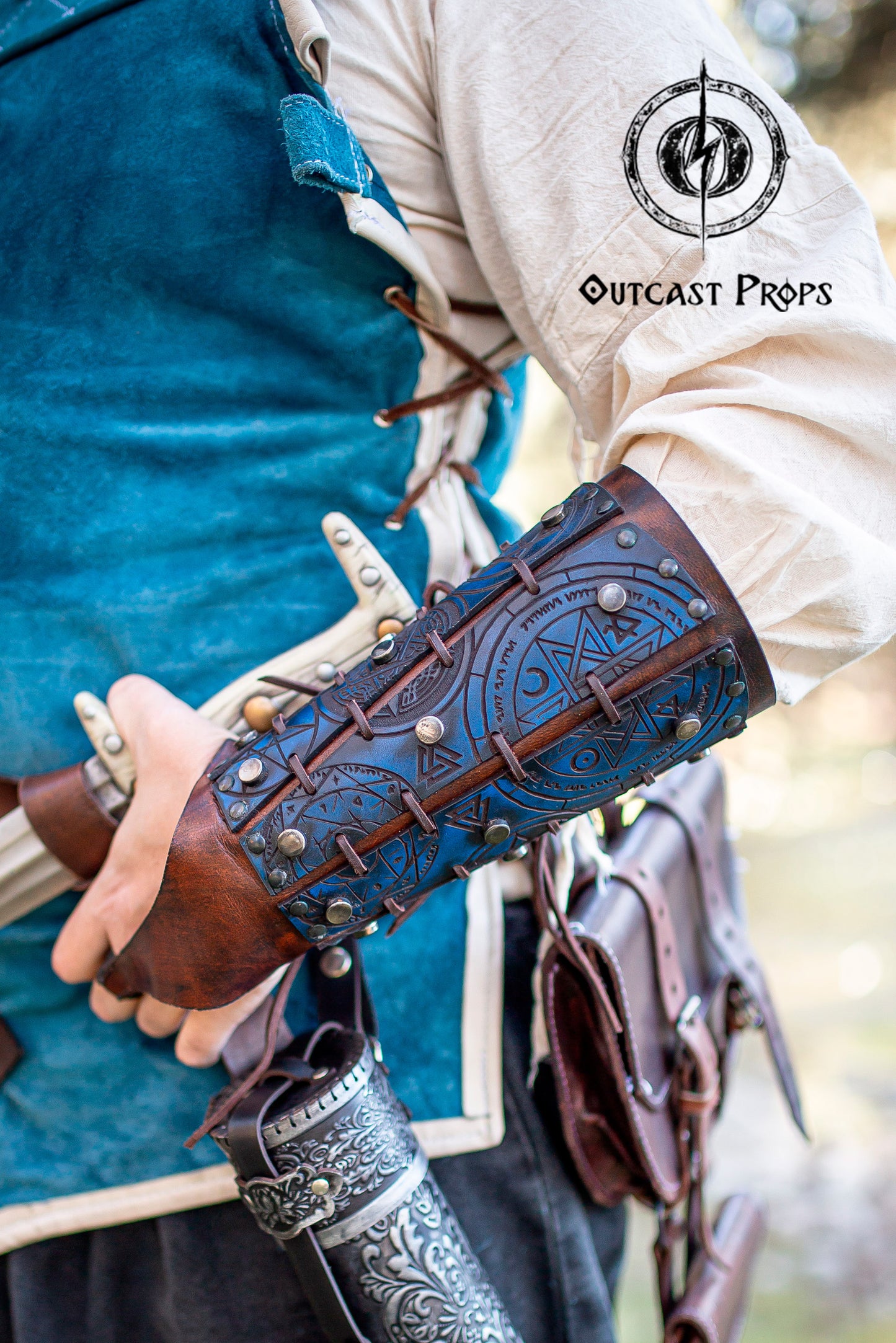 Detailed view of blue rune bracer worn by a fantasy adventurer with sword, scroll holder and belt accessories. Perfect LARP costume armor for alchemists, witch hunters, or steampunk characters. Handcrafted with engraved protection sigils, premium Spanish leather and epic weathered finish. Adjustable and practical for active cosplay or medieval reenactment.