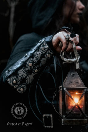 Female hand holding a lantern while wearing silver rune bracer with gothic engravings. Scene evokes mystery and magic, ideal for LARP witches, dark sorceresses, or fantasy rogues. Made with thick leather and aged painting technique, this handcrafted bracer offers full mobility, symbolic power and visual storytelling for immersive fantasy costumes.