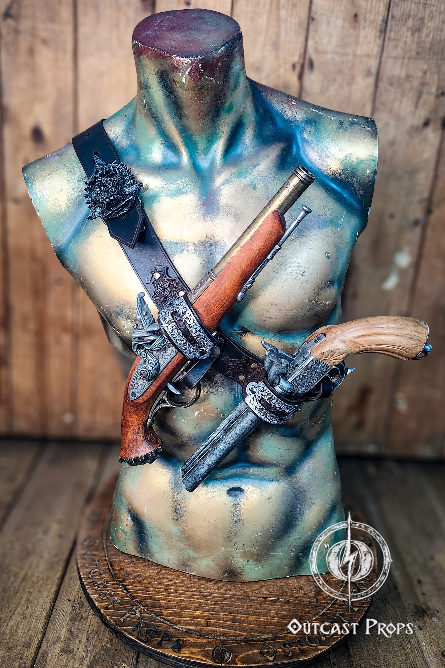 Mannequin torso wearing a handcrafted leather baldric inspired by Edward Kenway from Assassins Creed Black Flag. Two ornate flintlock pistols are crossed over the chest, held by engraved silver holsters. This pirate leather holster is ideal for LARP, pirate cosplay, or Caribbean rogue costumes. The rugged torso and wooden base enhance the adventurous, battle-worn look.