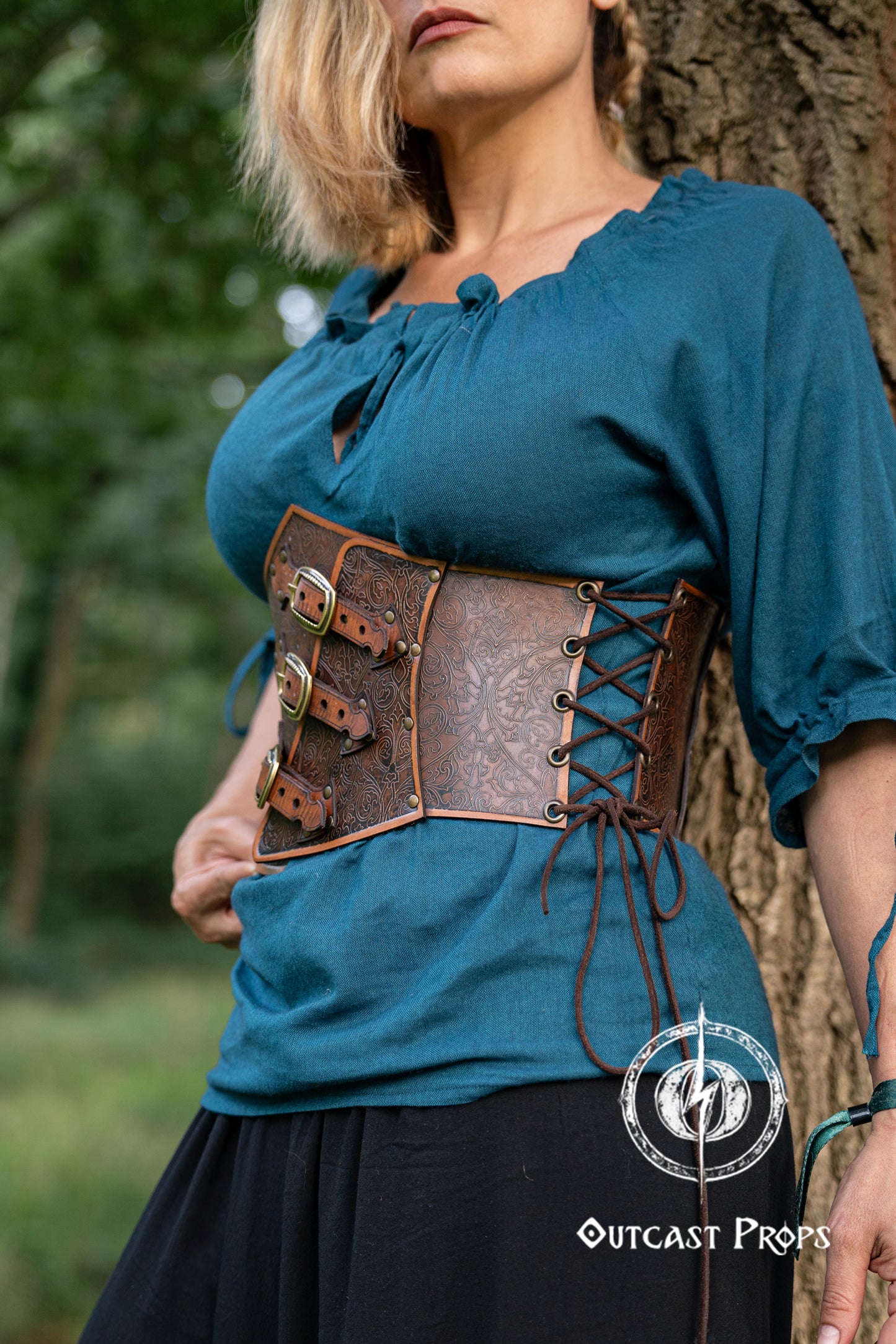 Woman wearing a teal top with a brown leather corset belt outdoors. Embroidered Leather Underbust Corset – Elegant Brown Waist Cincher for Noble LARP Outfits, Steampunk and Fantasy Glamour