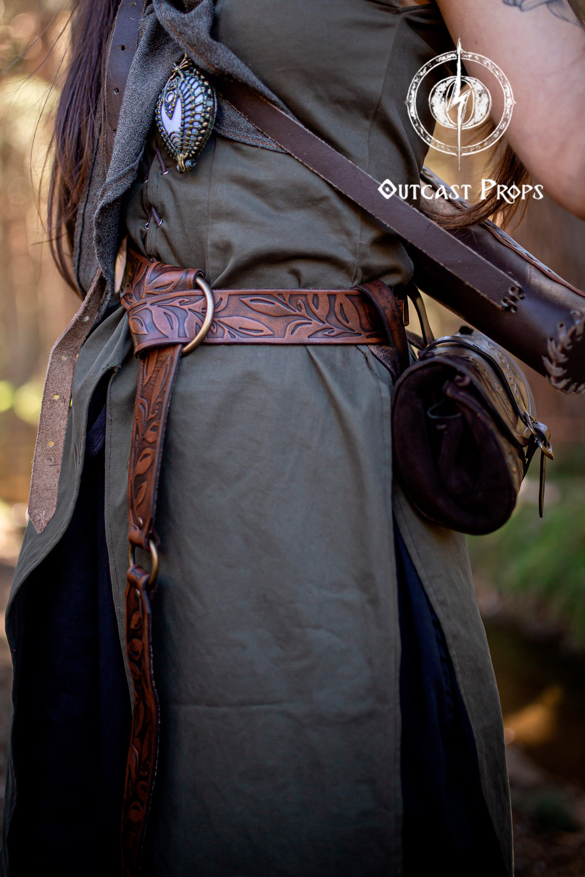 Close-up of a fantasy elven costume featuring a brown Floral Leather Belt with O-Rings worn over a green medieval-style dress. A small leather pouch hangs from the belt, and a hand-wrapped stone pendant is visible on the chest. Ideal for Renaissance Leather Belt with O Rings Fantasy Elven Waist Belt setups for Ren Faire or LARP. Handmade with vegetable-tanned leather, showcasing leaf tooling and rustic elegance.