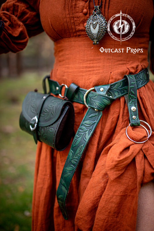 Close-up of a fantasy elven costume featuring a brown Floral Leather Belt with O-Rings worn over a green medieval-style dress. A small leather pouch hangs from the belt, and a hand-wrapped stone pendant is visible on the chest. Ideal for Renaissance Leather Belt with O Rings Fantasy Elven Waist Belt setups for Ren Faire or LARP. Handmade with vegetable-tanned leather, showcasing leaf tooling and rustic elegance.