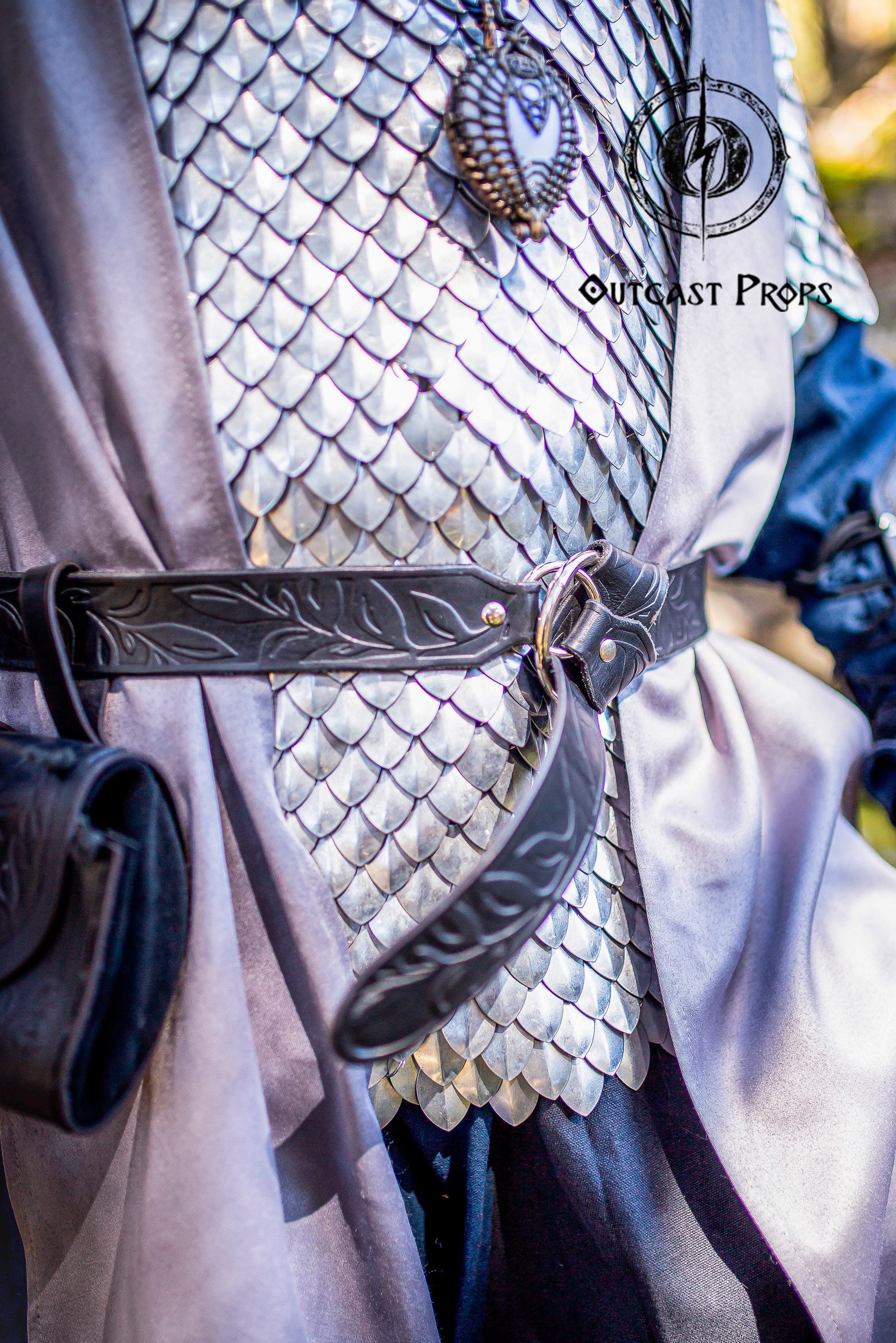 Close-up of a Fantasy Elven LARP Belt worn over shiny silver scale armor and a flowing gray cloak. The black Floral Leather Belt with O-Rings adds a powerful medieval touch, ideal for Ren Faire Medieval Cosplay Waist Belt looks. Hand-tooled with elegant leaf motifs on vegetable-tanned leather, this belt brings fantasy elegance and rugged functionality to warriors, knights, or adventurers.
