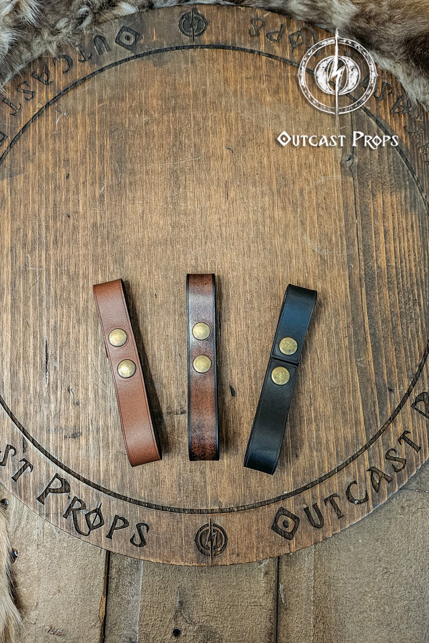 Leather belt pair of clasp mug holder belt strap medieval accessory set of two for LARP cosplay renaissance fair Handcrafted Vegetal Tanned. Three leather straps with metal fasteners on a wooden surface with 'Outcast Props' branding.