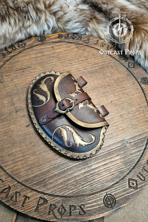 Small renaissance noble pouch made of brown aged leather with golden painted edges and floral curves. The pear shape bag rests on rustic wooden surface surrounded by fur. It includes a brass buckle and hand-laced seams, showing Outcast Props’ unique aging techniques. Ideal for LARP pouch lovers, medieval fairs, and fantasy costume accessories handmade in Spain.