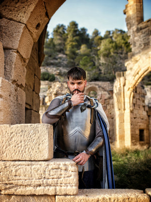 Fantasy knight posing in front of ancient ruins, wearing elegant steel armor and decorated leather bracers with engraved metal plates. His confident stance and detailed outfit make this perfect for epic knight cosplay, noble LARP roles, and fantasy storytelling. The ruined background adds historic depth.