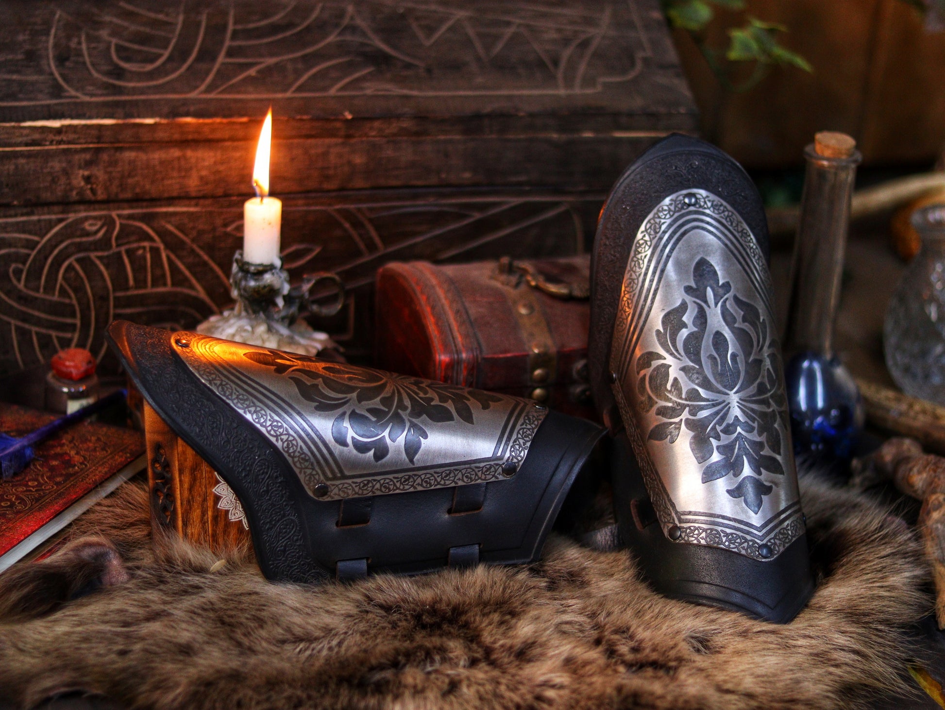 Bracers with engraved steel plates and black leather resting on fur beside a carved chest and candle. The perfect mix of noble elegance and fantasy gear, ideal for medieval roleplay, knight costumes, or detailed cosplay props. Rich warm tones enhance the immersive, handcrafted feel.