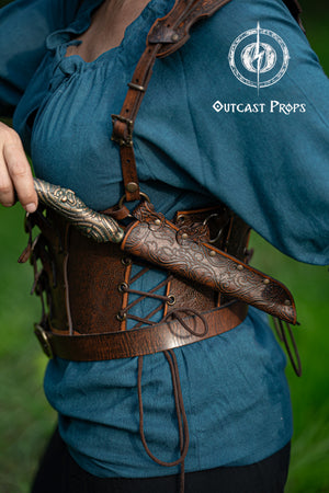 Ornated Magic Wand shoulder Holster full-grain leather with potions for wizards and witches. Dark Academy style. MACUSA Cosplay and LARP. A person wearing a white shirt and a shoulder holster in a patterned fabric. The holster is brown, made of leather, and designed to hold a wand.