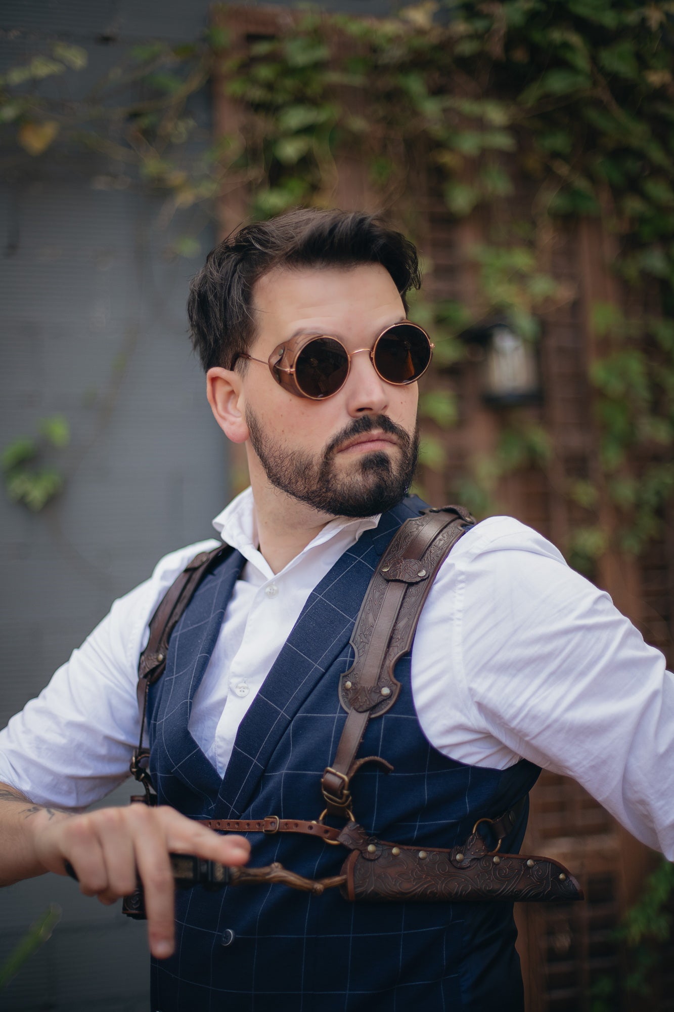 Ornated Magic Wand shoulder Holster full-grain leather with potions for wizards and witches. Dark Academy style. MACUSA Cosplay and LARP. A person wearing a white shirt and a shoulder holster in a patterned fabric. The holster is brown, made of leather, and designed to hold a wand.