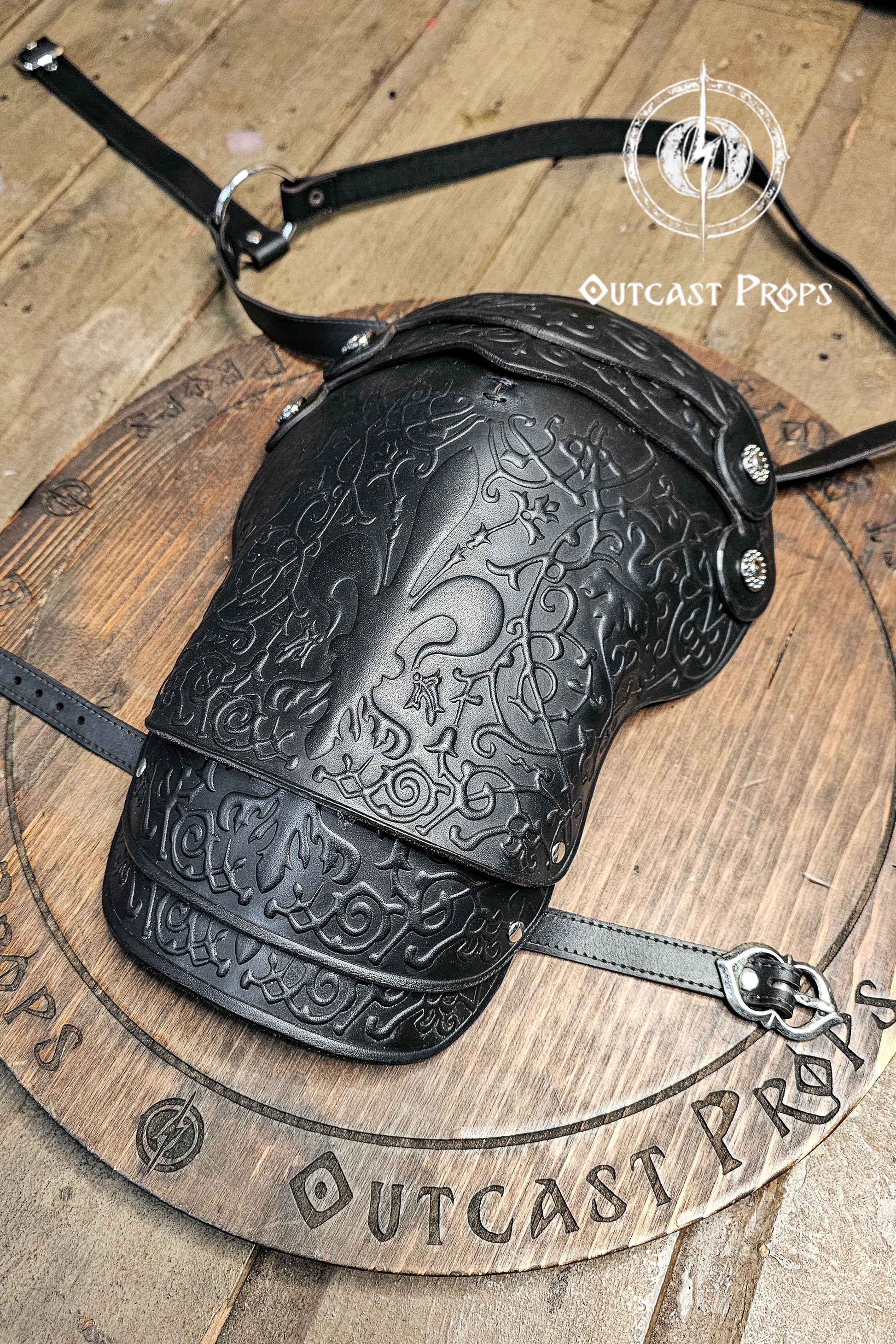 Decorative black arm guard on a wooden surface with 'Outcast Props' branding. Leather Shoulder Pauldron: Musketeer Armor for LARP, Renaissance LARP, cosplay, Ren Faire accessory, Aramis inspired