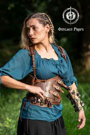 Person wearing steampunk-style clothing with Outcast Props logo in the corner. A handmade leather potion holder with ornate embossed patterns, designed to hold five small glass vials. The holder is displayed on a furry surface, and the vials have cork stoppers. Ornated Belt potion holder | 5 potion Belt carrier | LARP, cosplay, fantasy alchemist accessory, adventurers, steampunk, alchemist, healers