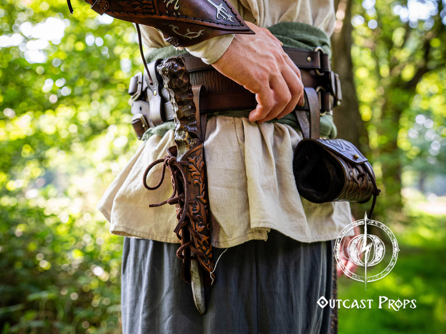 Person wearing historical or fantasy costume with props in a forest setting. Handmade leather dagger sheath | Ornate LARP scabbard | Viking, medieval, fantasy belt holster for daggers | Ren Faire cosplay accessory