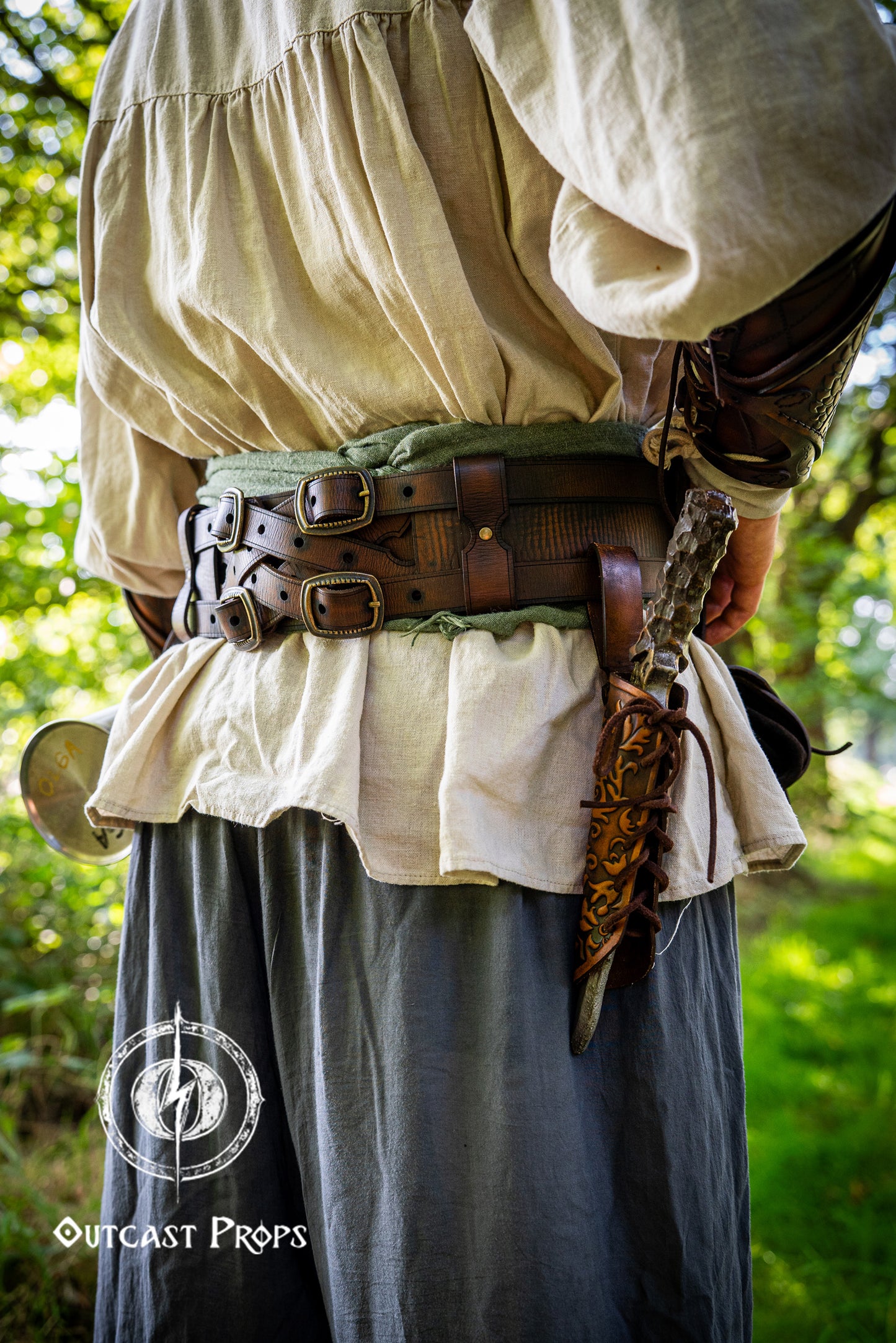 Person wearing historical clothing with a belt and sword, standing in a forest. Handmade leather dagger sheath | Ornate LARP scabbard | Viking, medieval, fantasy belt holster for daggers | Ren Faire cosplay accessory