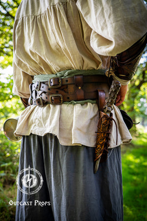 Person wearing historical clothing with a belt and sword, standing in a forest. Handmade leather dagger sheath | Ornate LARP scabbard | Viking, medieval, fantasy belt holster for daggers | Ren Faire cosplay accessory