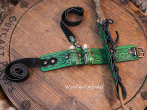 Top-down view of a green embossed leather garter for magic cosplay accessories, laid on a wooden background. Two potion bottles are held in custom loops, and a wand (not included) is secured in a lace-wrapped holster. Adjustable black leather straps allow it to fit around the leg. This is perfect for female wizard cosplay, witch potion garter, or herbalist LARP gear.
